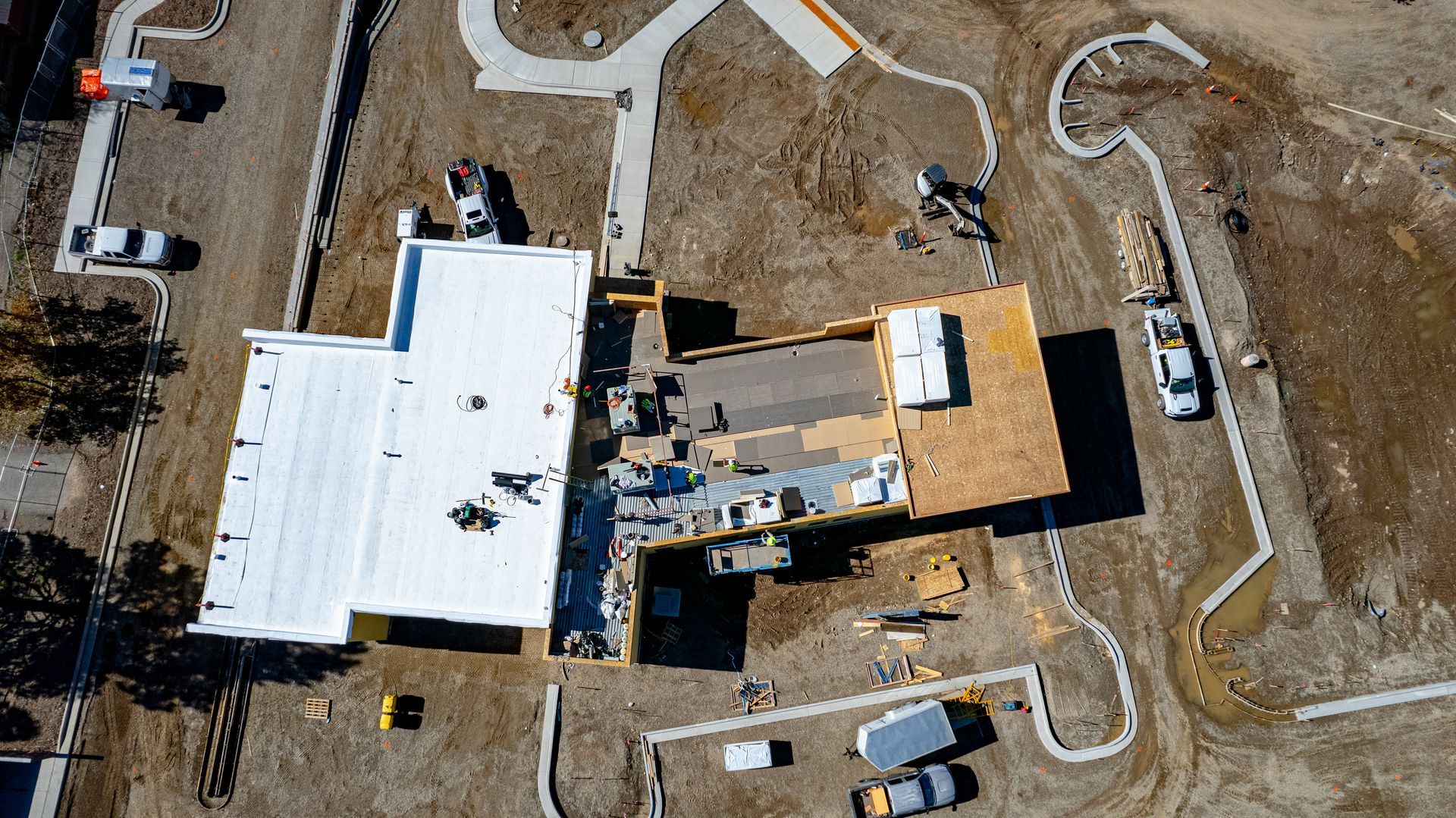 Overhead view of a construction site showing a white roof, exposed wall framing and curved concrete sidewalks.