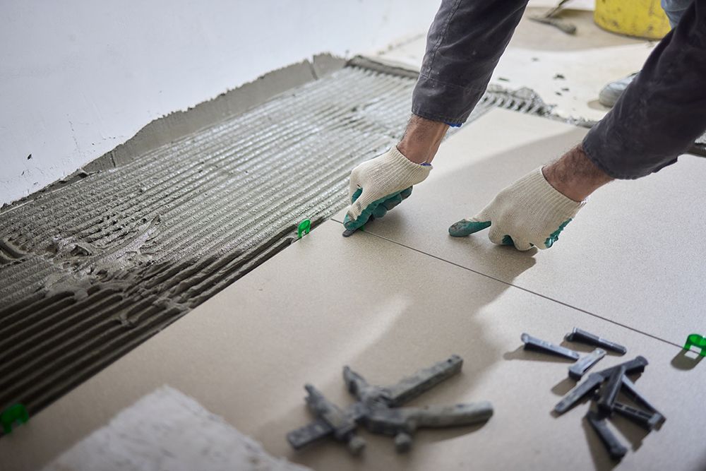A man is laying tiles on the floor with a trowel.