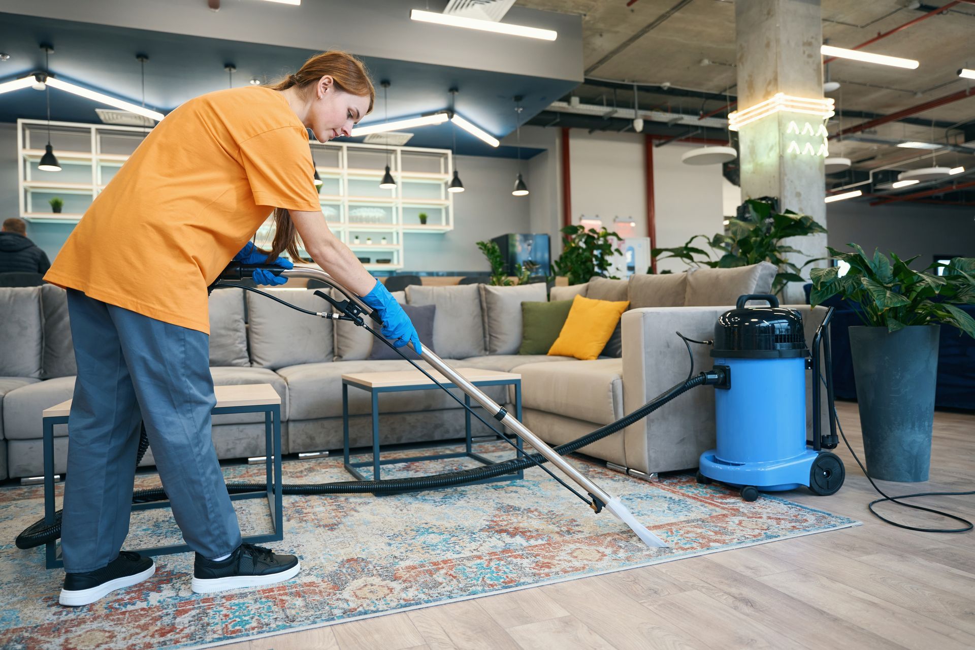 A woman from a cleaning company in a comfortable uniform cleans the carpet.