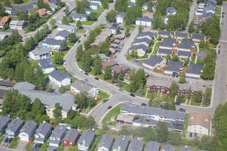 Aerial view of a suburban neighborhood with curving streets, houses, trees, and parked cars