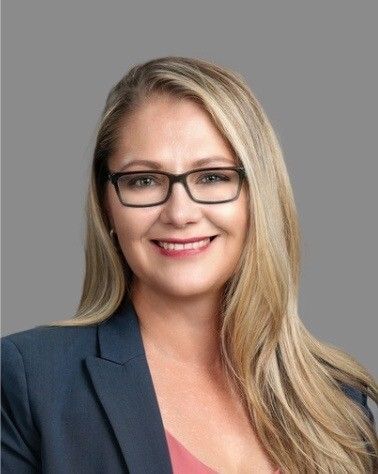 Smiling professional woman with glasses in a dark blazer against a gray background