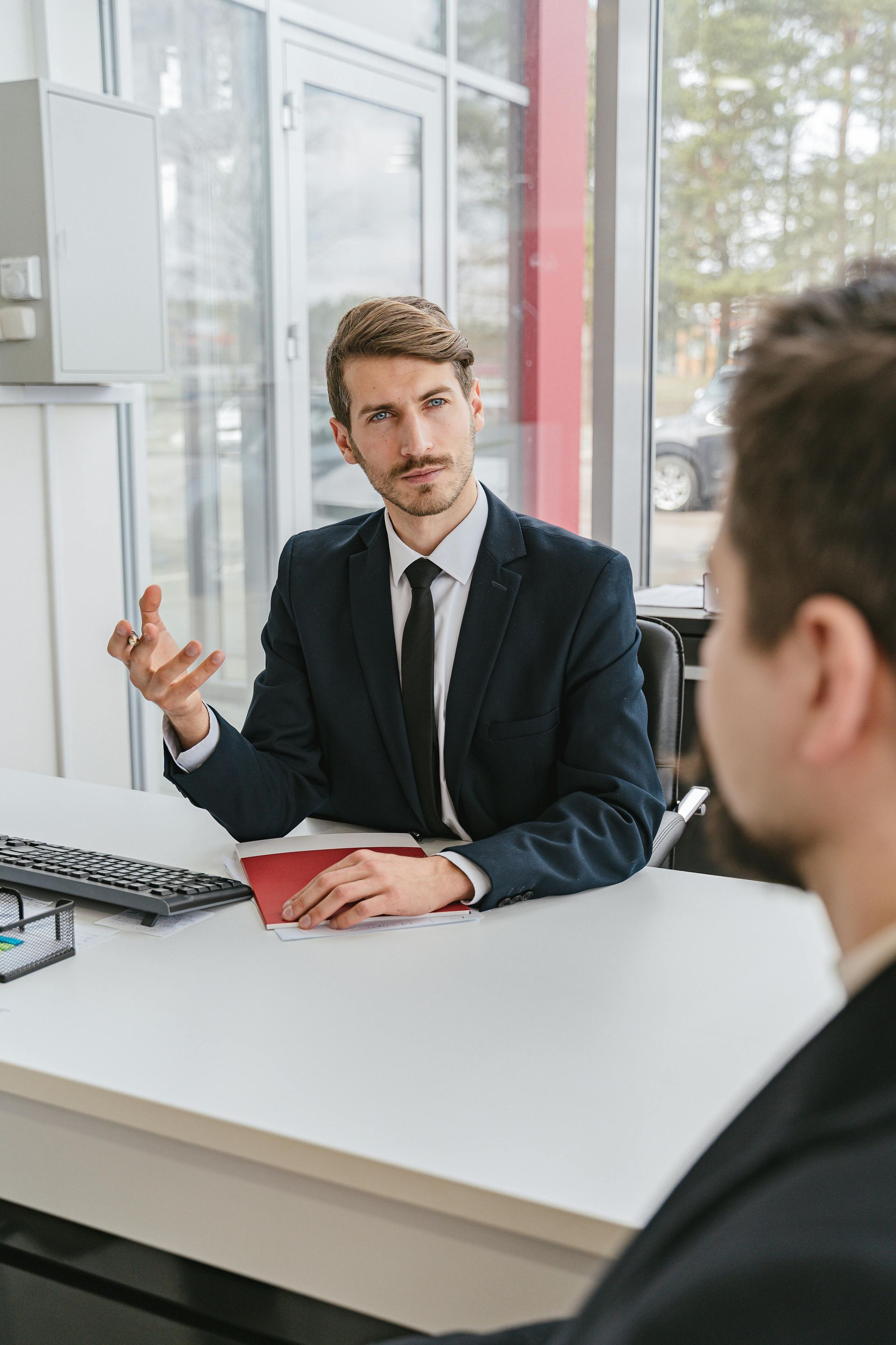 Business meeting at a desk, with one man speaking to another in an office setting.