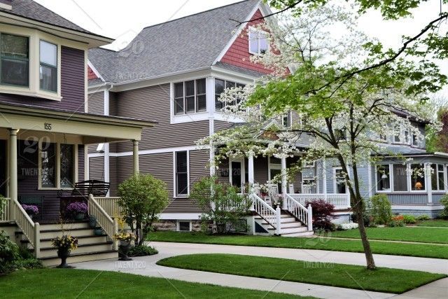 Row of gray beach houses with white trim and porches along a green lawn and sidewalk
