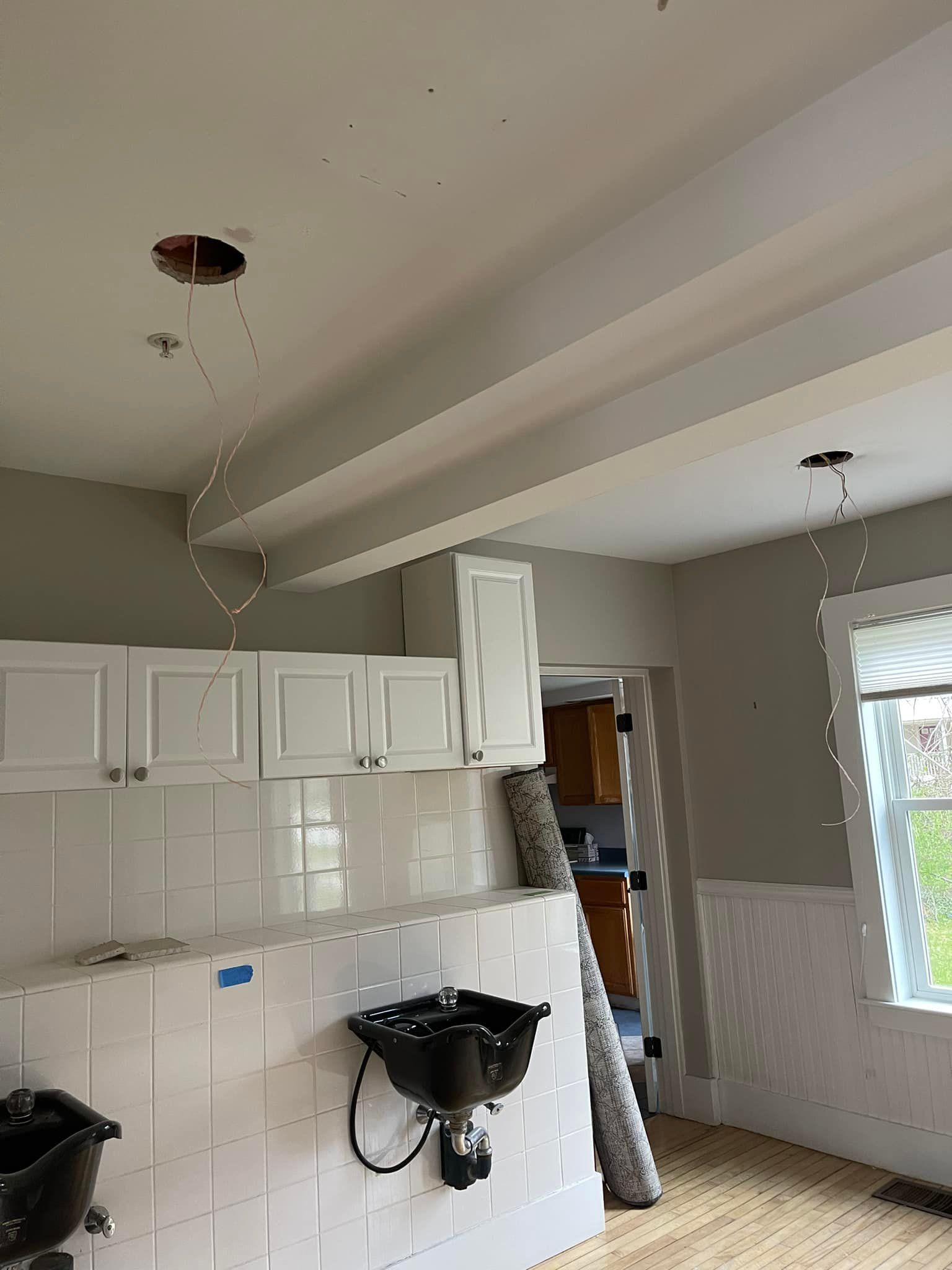 Kitchen under construction with white cabinets, tiled backsplash, black sinks, and exposed ceiling wires.