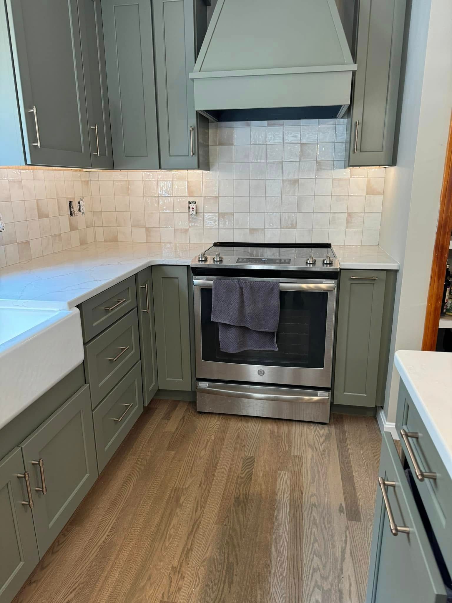 Sage green kitchen with white countertops, stainless steel appliances, and tiled backsplash.