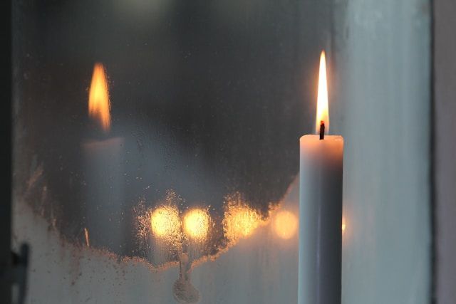 Single lit candle by window with soft reflections, symbolizing remembrance, cremation services Middletown, PA