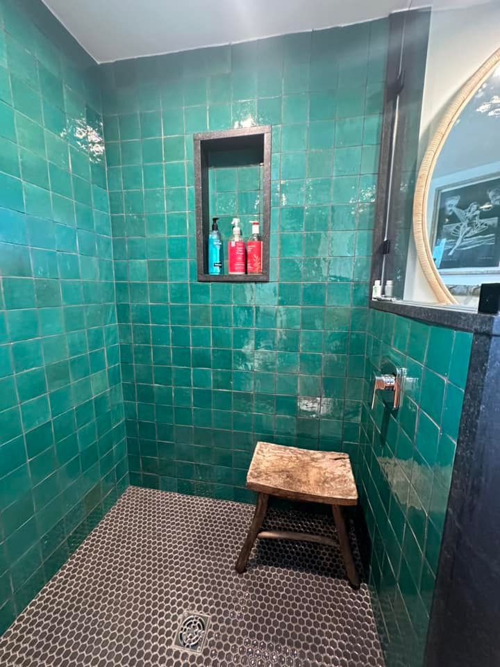 Green tiled shower with a small wooden stool and a built-in shelf with toiletries.