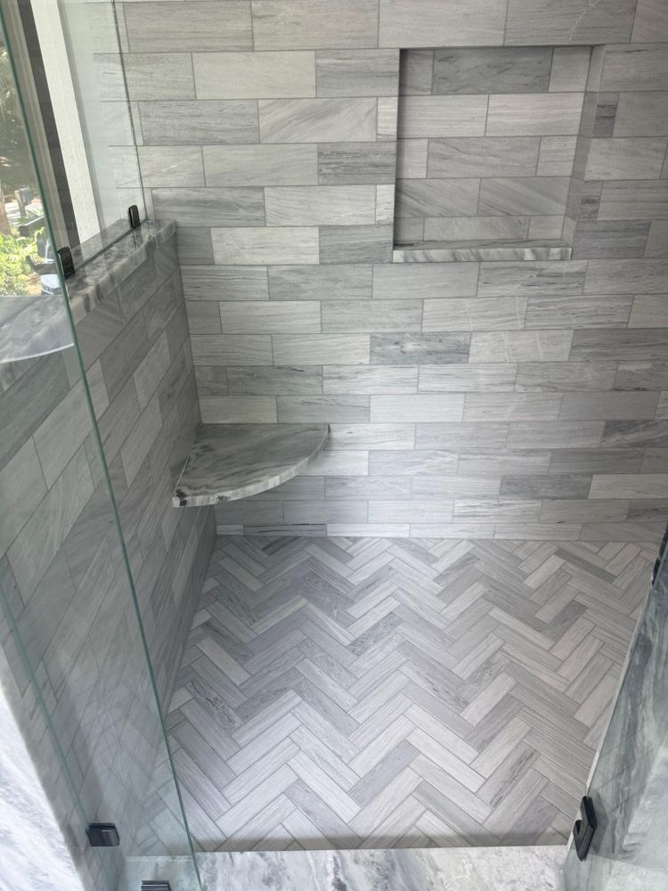 Shower with gray herringbone floor tile, gray wall tiles, glass doors, and a built-in shelf.