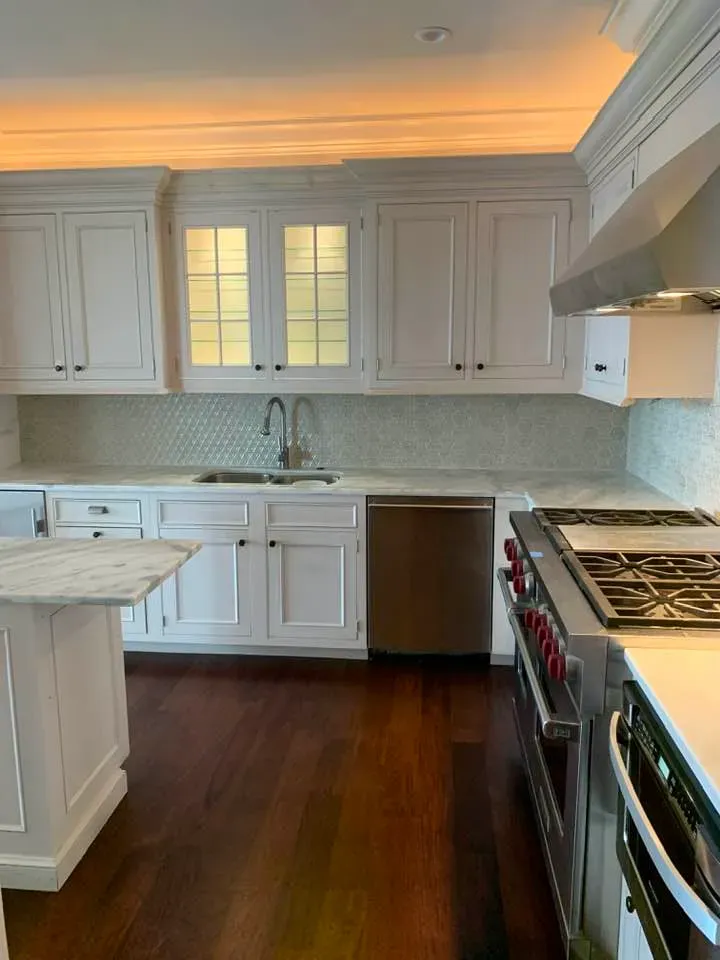 White kitchen with marble countertops, stainless steel appliances, and dark wood floors.