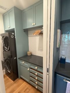 Small laundry room with blue cabinets, stacked washer/dryer, and a dark countertop.