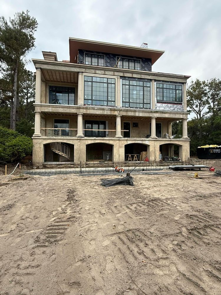 A multi-story beige house under construction; featuring columns, large windows, and a flat roof.
