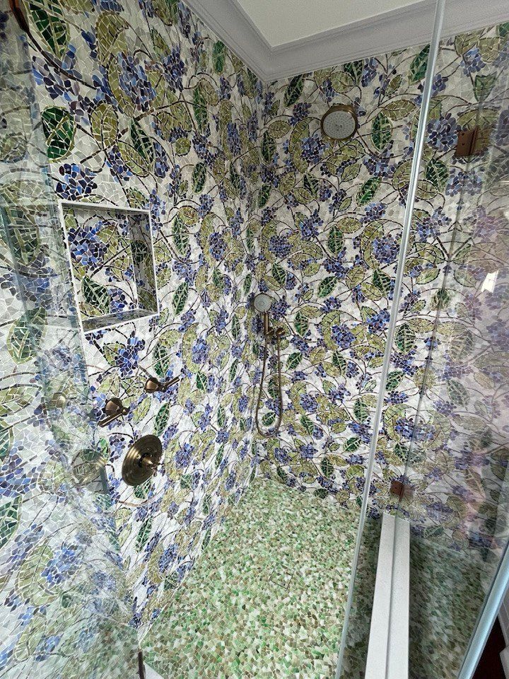 Shower with floral-patterned tiles in blue, green, and white. Glass door. Green tiled floor.