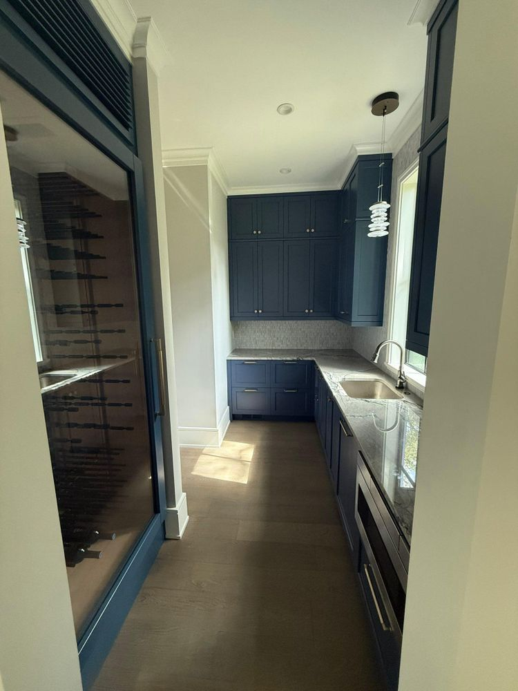 Dark blue cabinetry and stainless steel sink in a narrow room with wine cooler on the left.