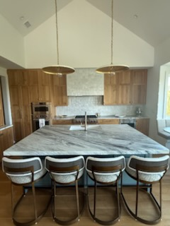 Kitchen with a large island, wood cabinets, and pendant lights. Four bar stools are in front of the island.