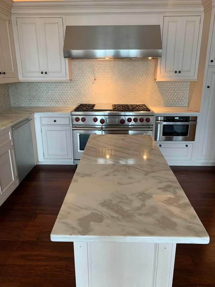 Kitchen with white cabinets, marble island, stainless steel appliances, and a mosaic backsplash.