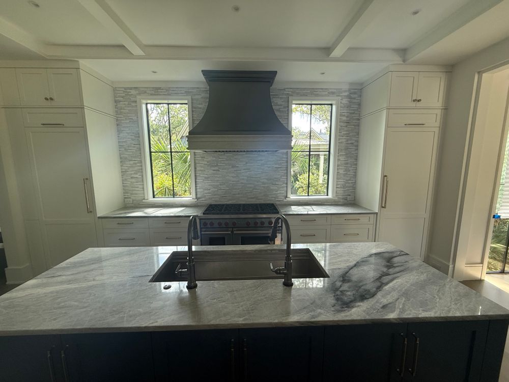 Kitchen with white cabinets, blue island, gray countertops, and a dark range hood.