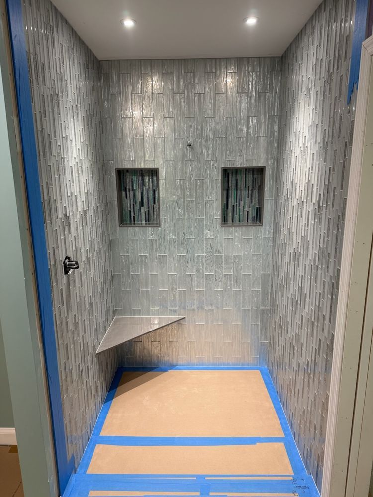 Newly tiled shower with built-in bench and two niches. Blue-gray textured tile, recessed lighting.