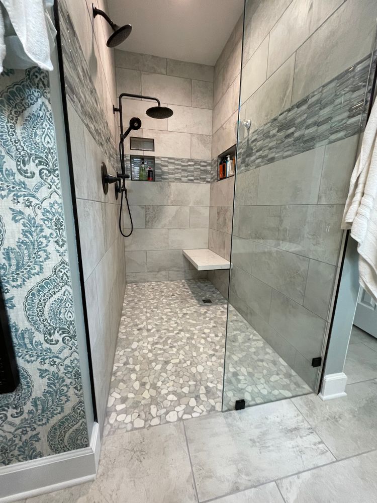Modern shower with pebble floor, gray tile walls, glass door, and black shower fixtures.