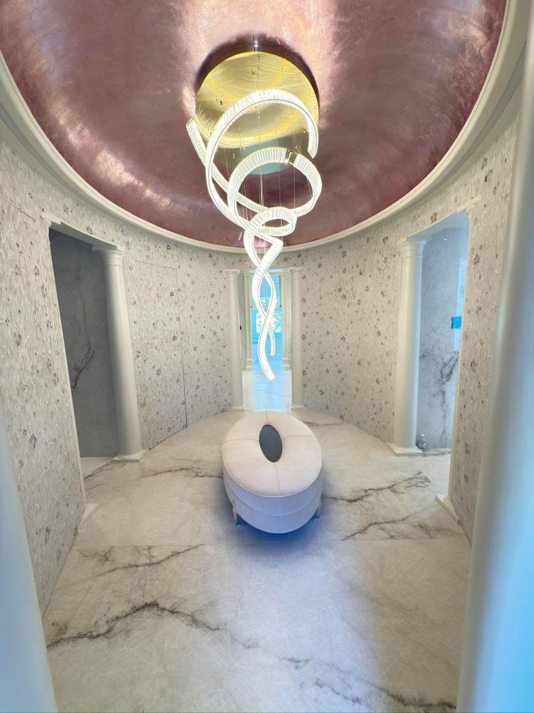 A luxurious spa room with a pink ceiling, marble floor, and a modern light fixture.