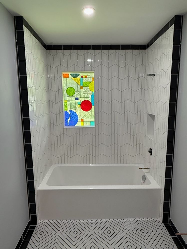 Bathroom with white tub, geometric tile walls, colorful art, and black trim.