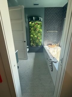 Bathroom with a large jar filled with green, eye-shaped objects. Includes tub, door, and tiled wall.
