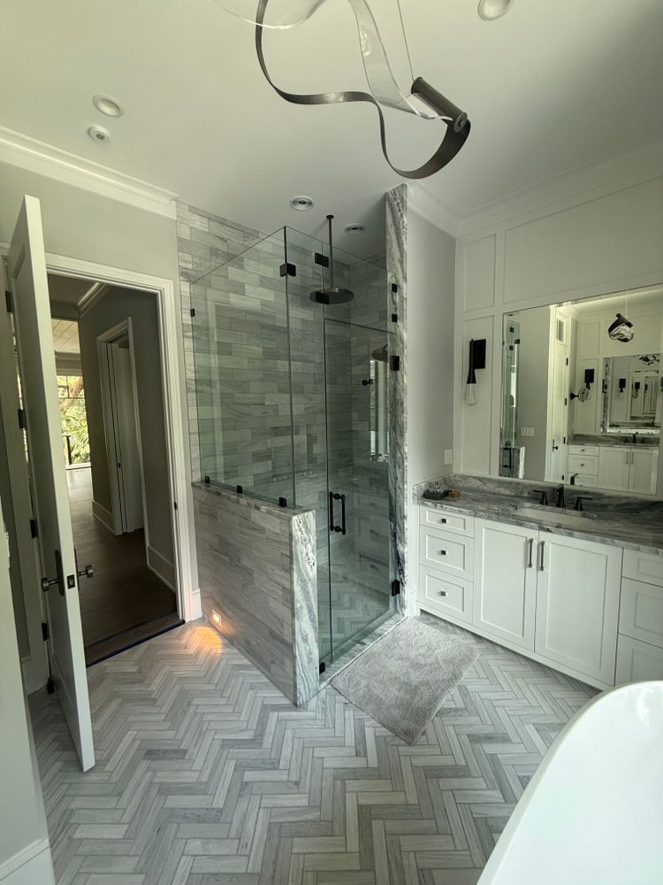 Modern bathroom with glass shower, white vanity, and herringbone tile floor.