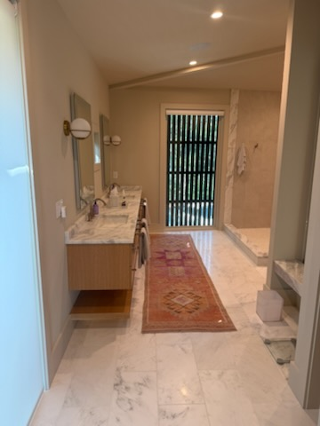 Bathroom with double vanity, marble floors, shower, and patterned rug.