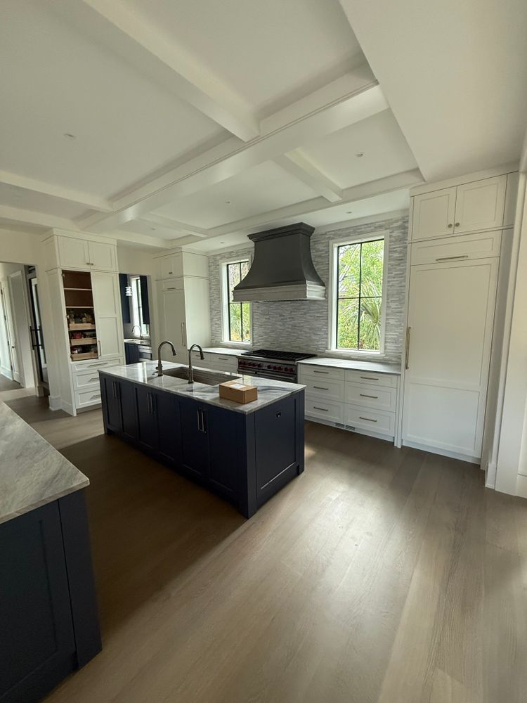 Modern kitchen with a navy island, white cabinets, stainless steel range hood, and light wood floors.