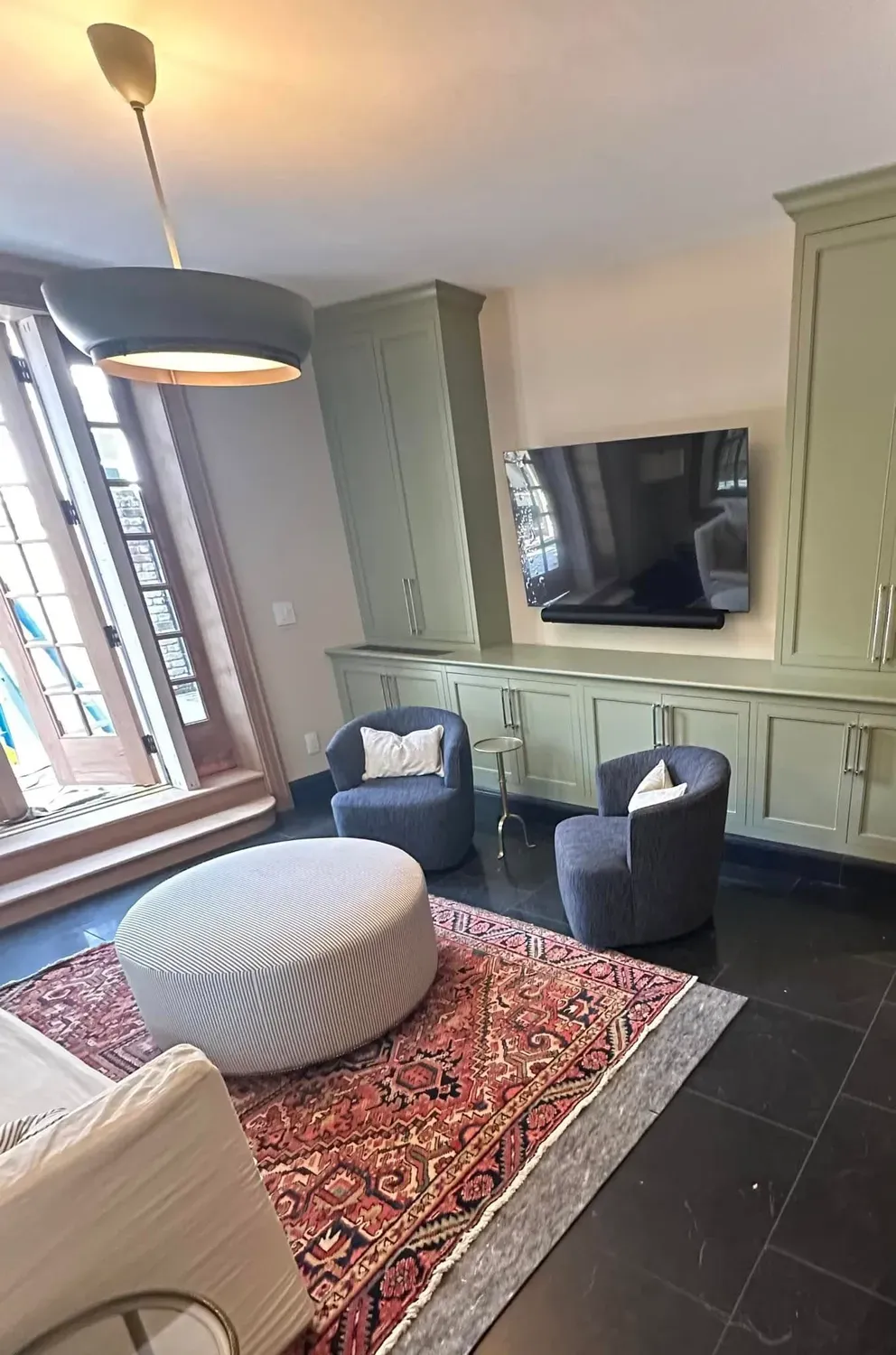 Living room with green cabinets, TV, two blue chairs, rug, and a round ottoman.