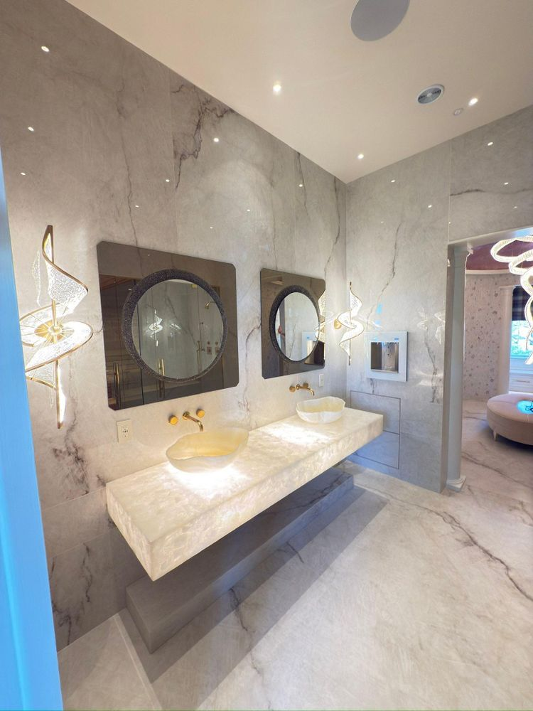 Luxurious bathroom with marble walls, floating sink, round mirrors, and decorative lighting.