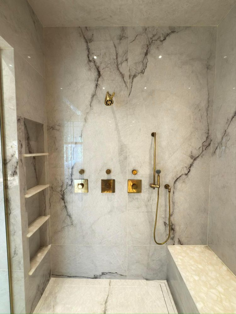 Luxurious marble shower with gold fixtures and built-in bench.