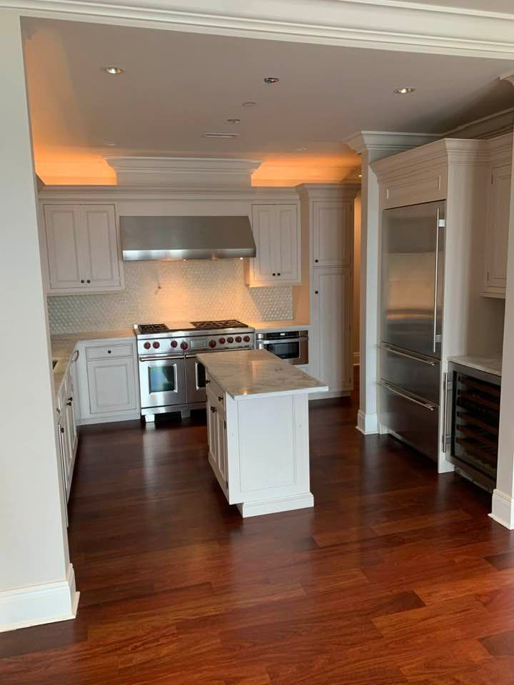 White kitchen with stainless steel appliances and dark wood floors.