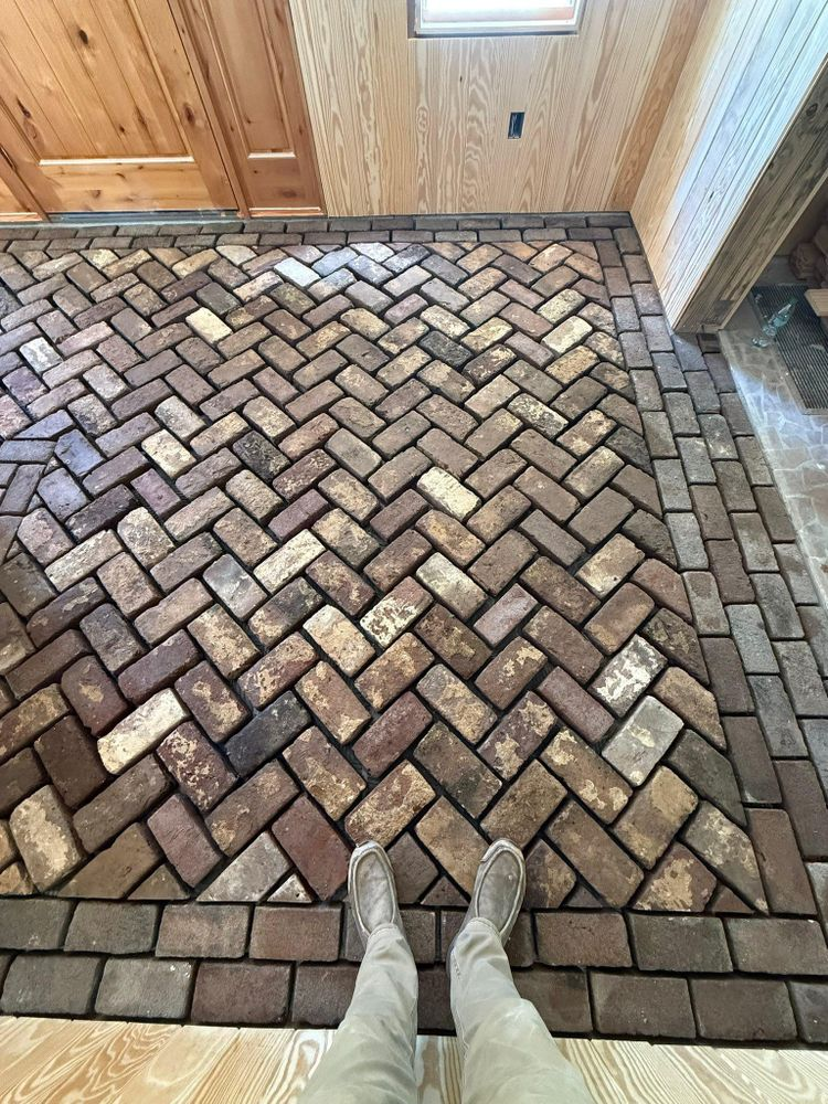 Person standing on a herringbone-pattern brick floor. The floor has a border of rectangular bricks. Wooden ceiling is above.