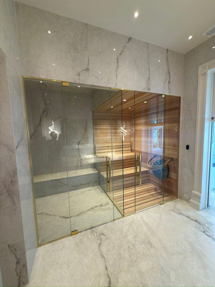 Luxury sauna with glass door, cedar wood interior, and marble tile walls and floor.