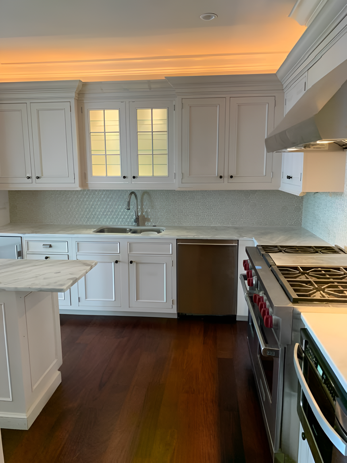 White kitchen with stainless steel appliances, marble countertops, and dark hardwood floors.