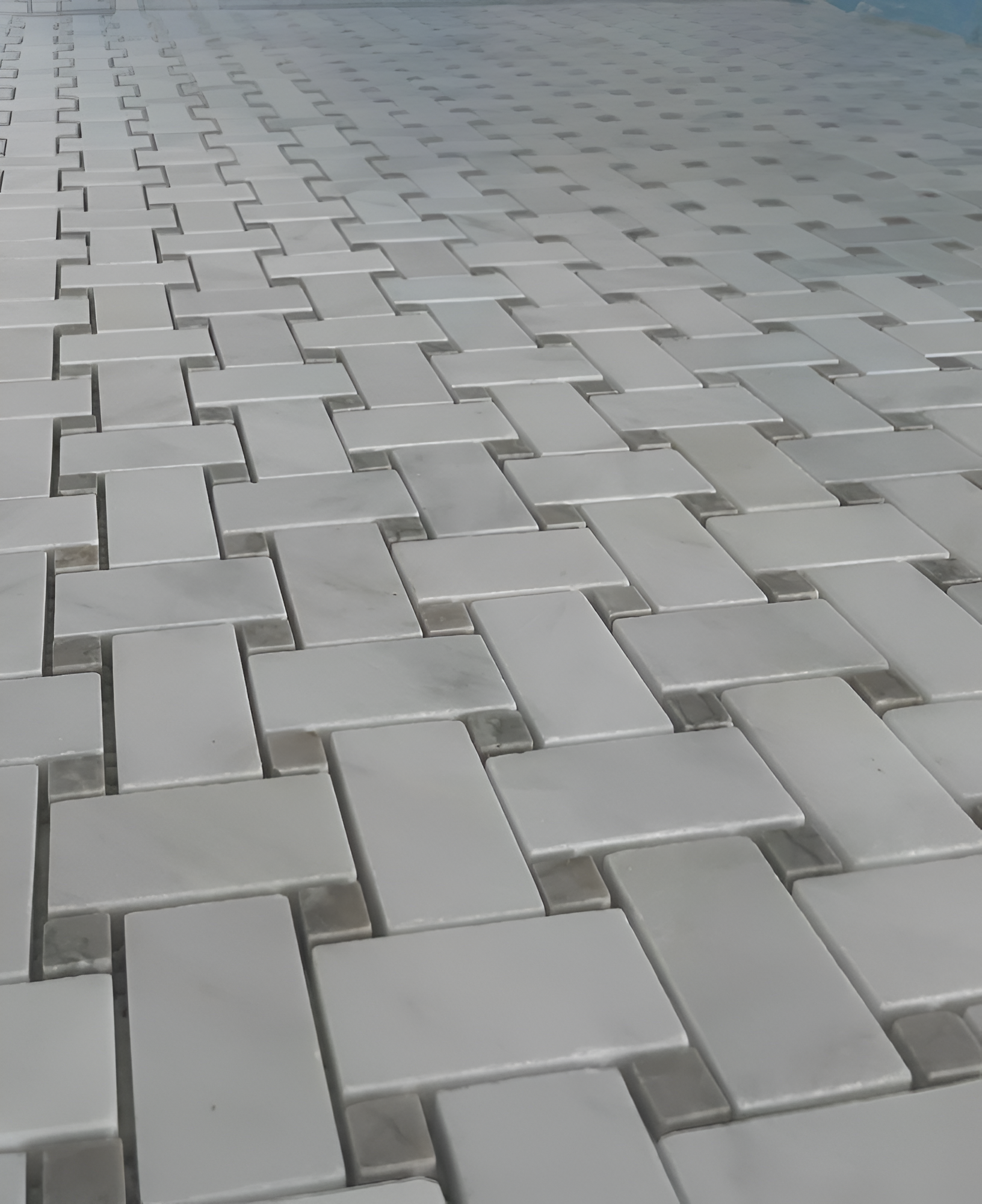Close-up of a floor tiled in a repeating pattern of light-colored rectangular blocks with darker connecting joints.