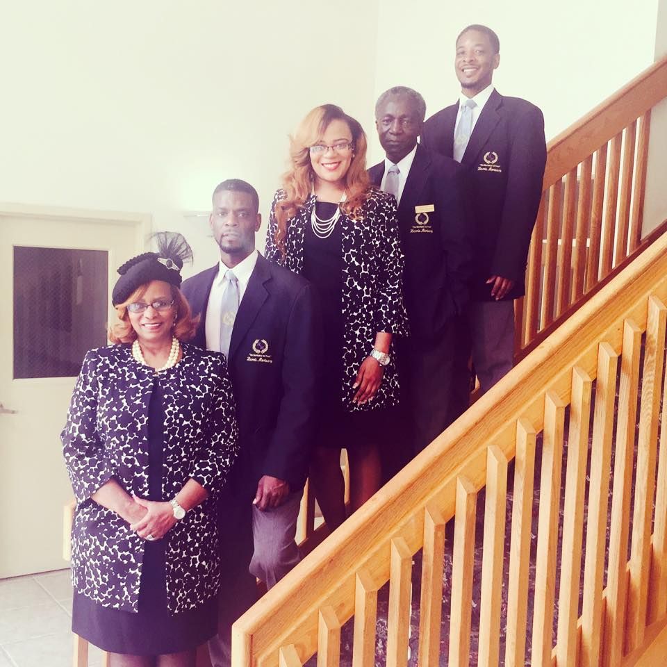 Five people in formal business attire pose on a wooden staircase indoors.