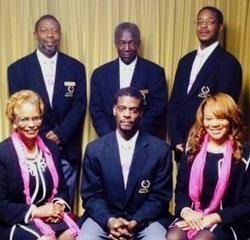 Group photo of five individuals in formal matching blazers and pink accessories, posing against a gold curtain backdrop.