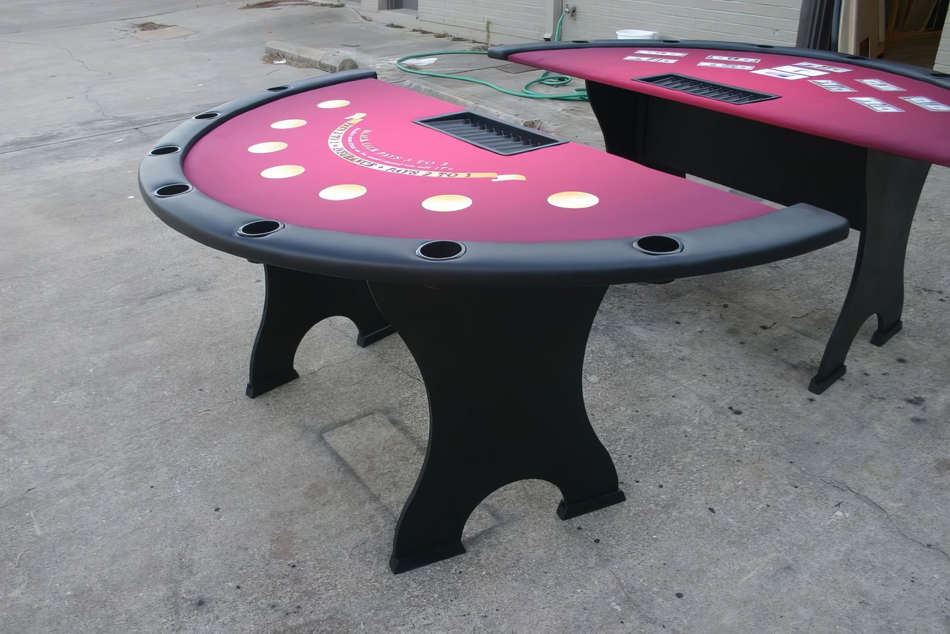 Two pink gaming tables with black legs on concrete, each with white card suit symbols around the edge