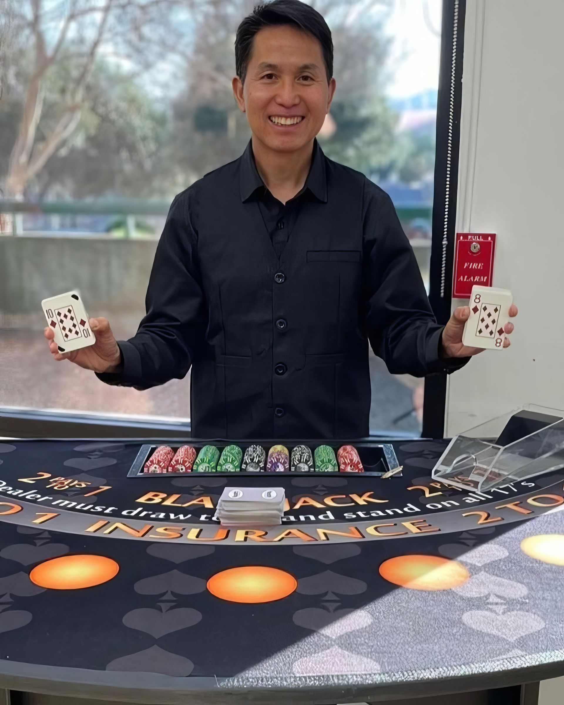Smiling dealer in black shirt holding cards behind a blackjack table at a casino table game