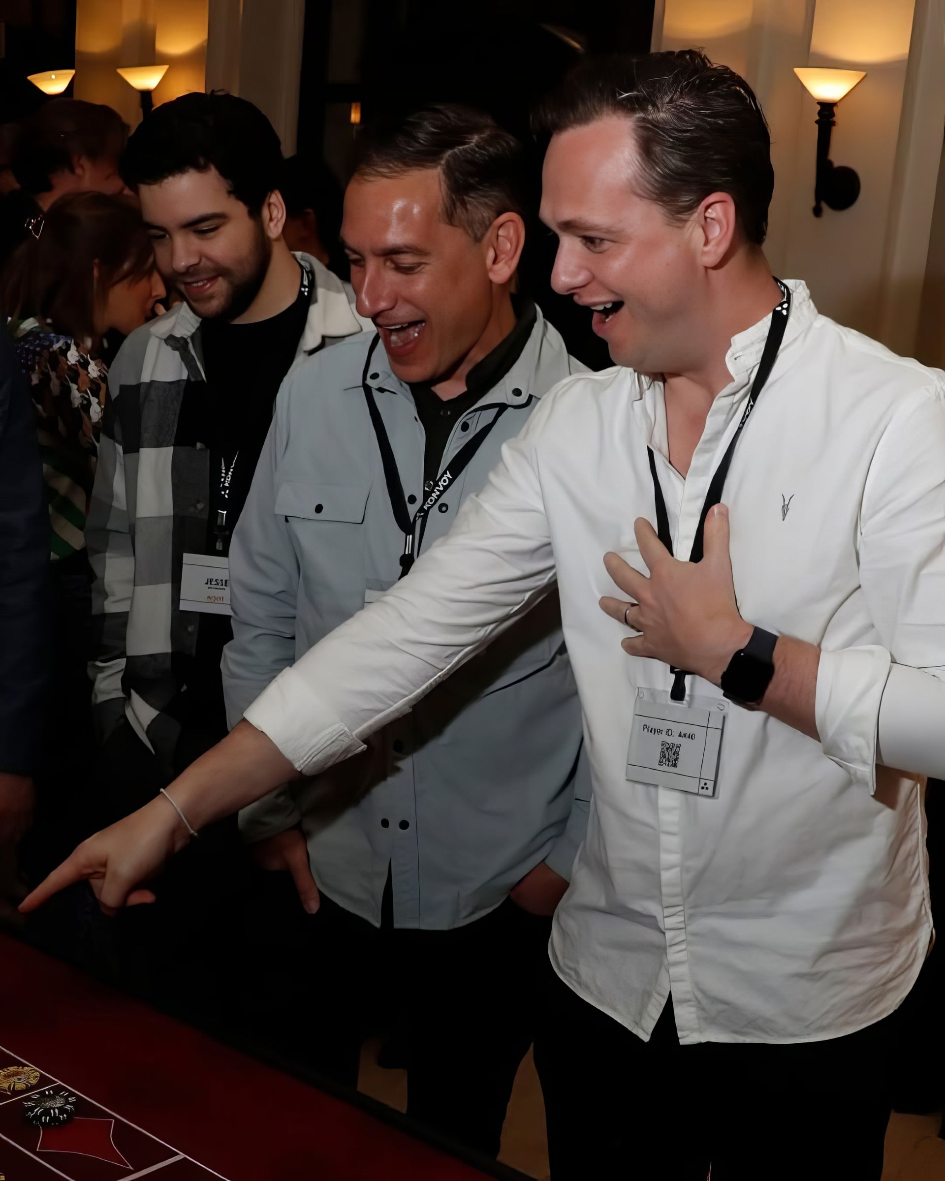 Three men in button-down shirts smiling and reaching toward a table at a dimly lit event