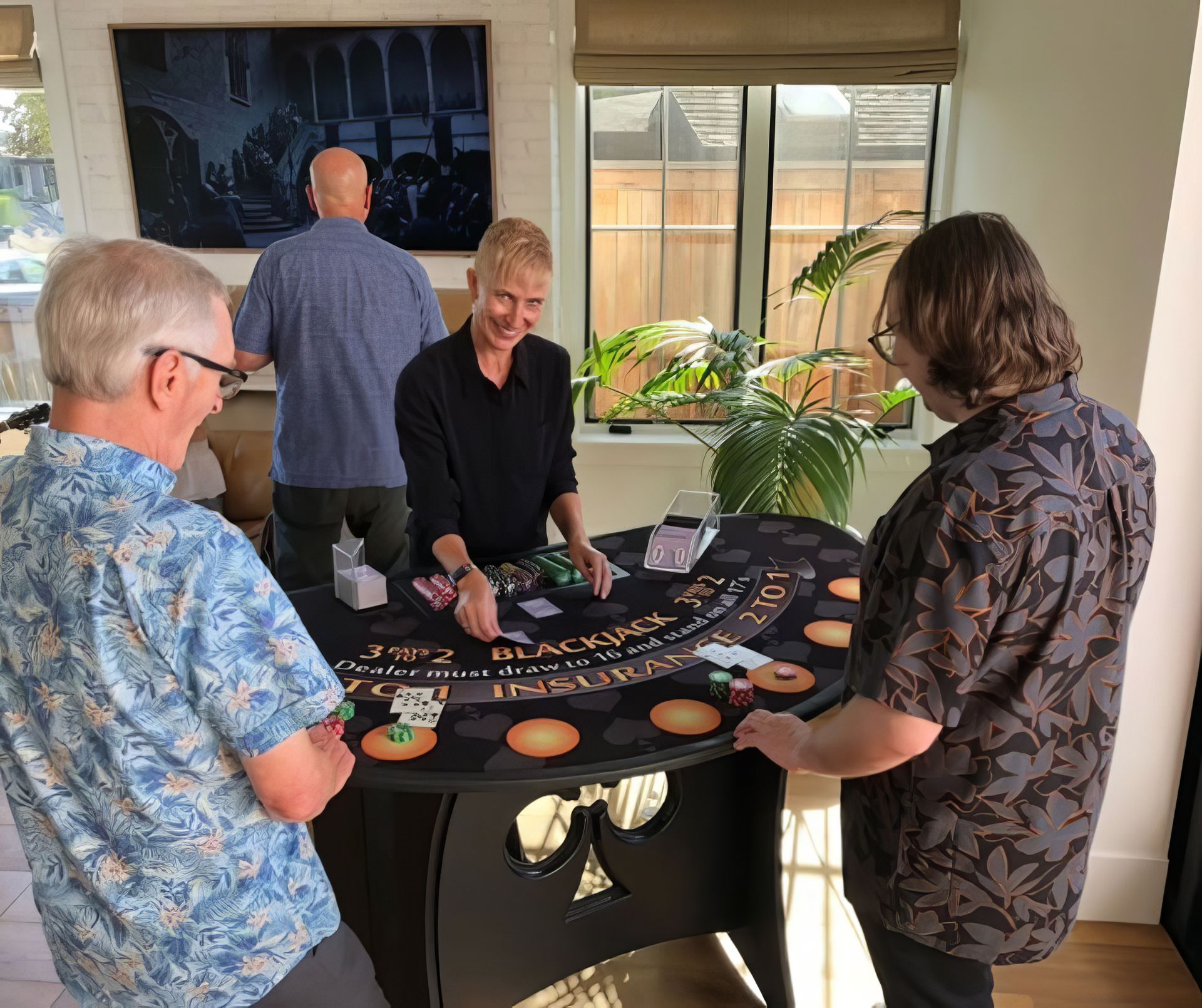 People gathered around a tabletop game in a bright living room near a window and TV.