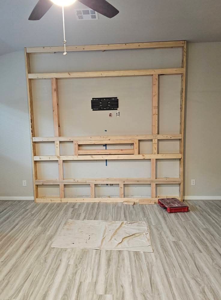 Un salon avec un centre de divertissement en bois et un ventilateur de plafond.