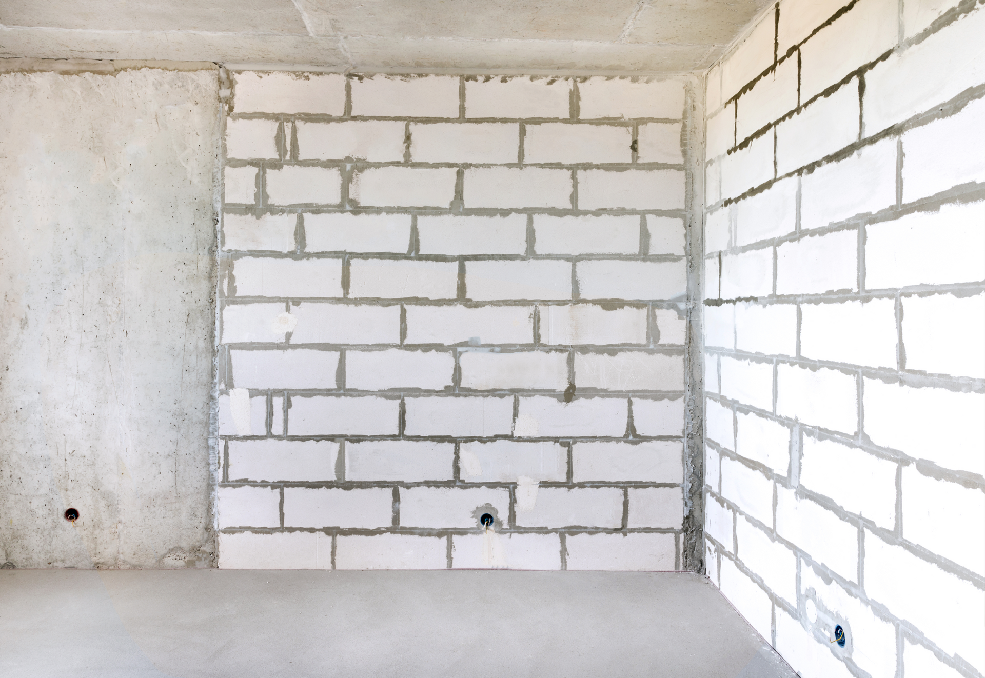 Une pièce vide avec des murs en briques blanches et un sol en béton.
