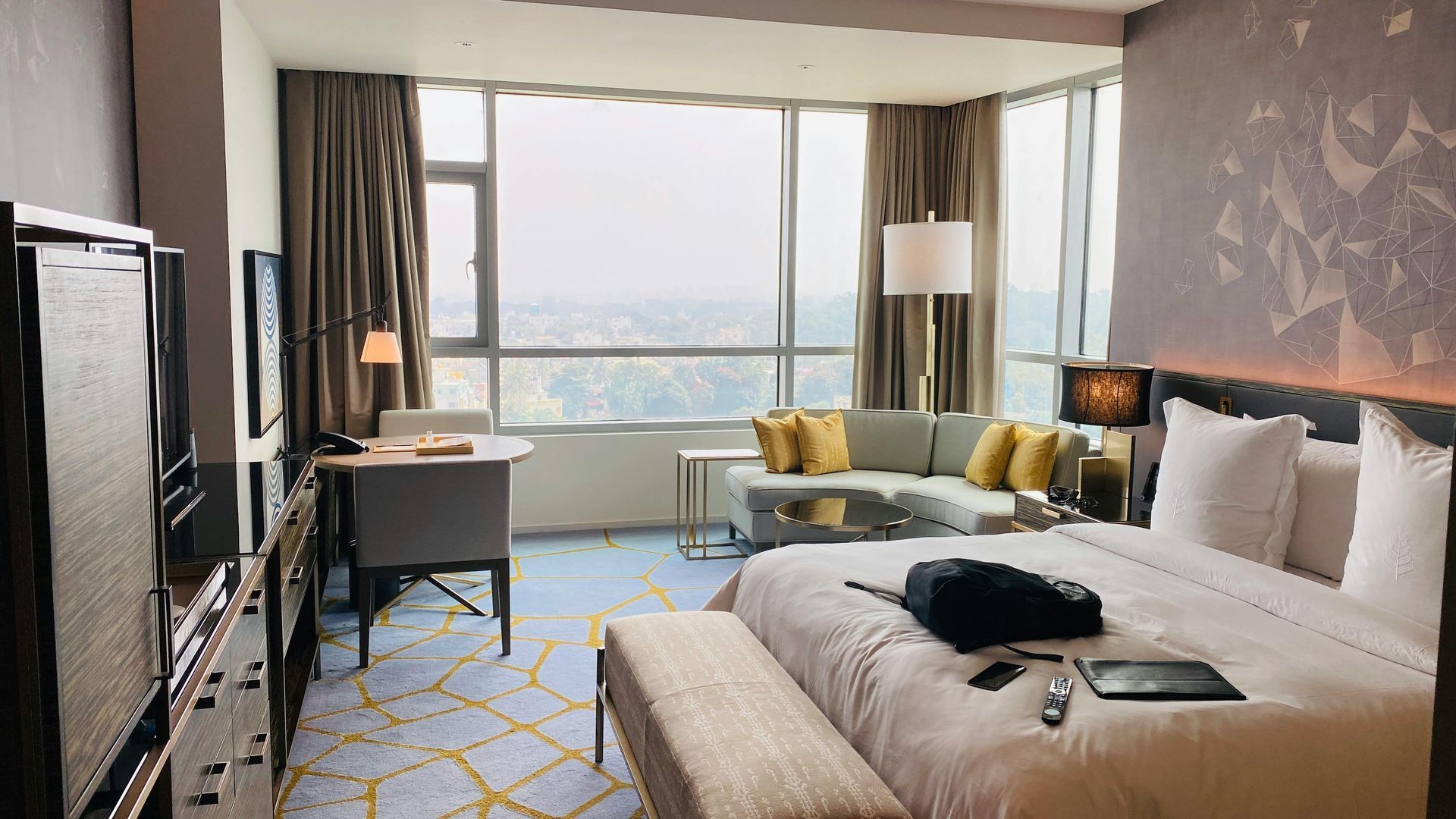 Suite d'hôtel avec lit, canapé, bureau, grandes fenêtres et vue sur la ville.