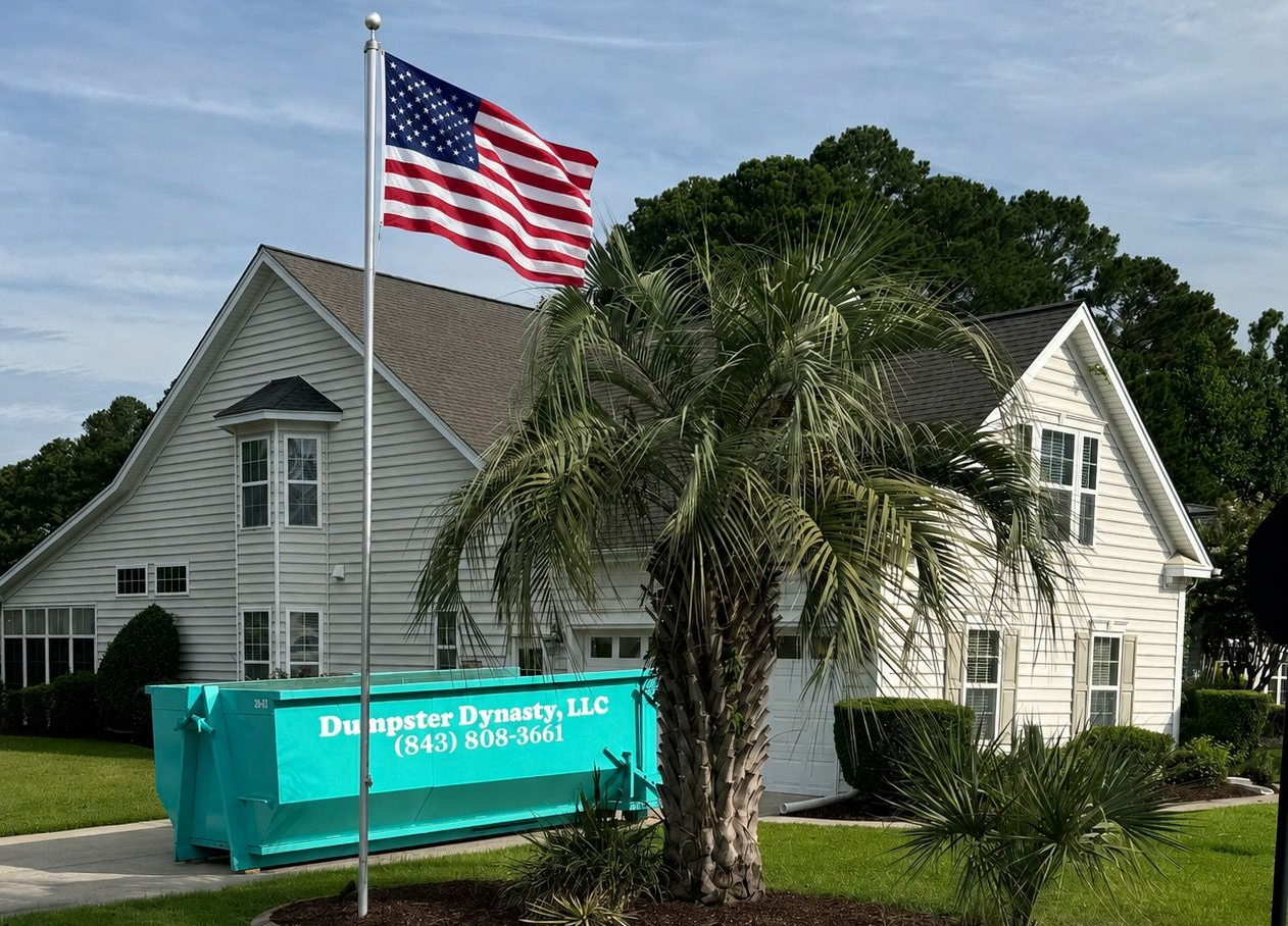 White house with American flag and palm tree beside a green dumpster in front yard