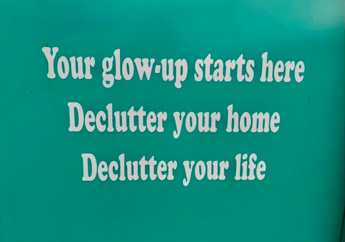Turquoise wall sign reading “Your glow-up starts here. Declutter your home. Declutter your life”