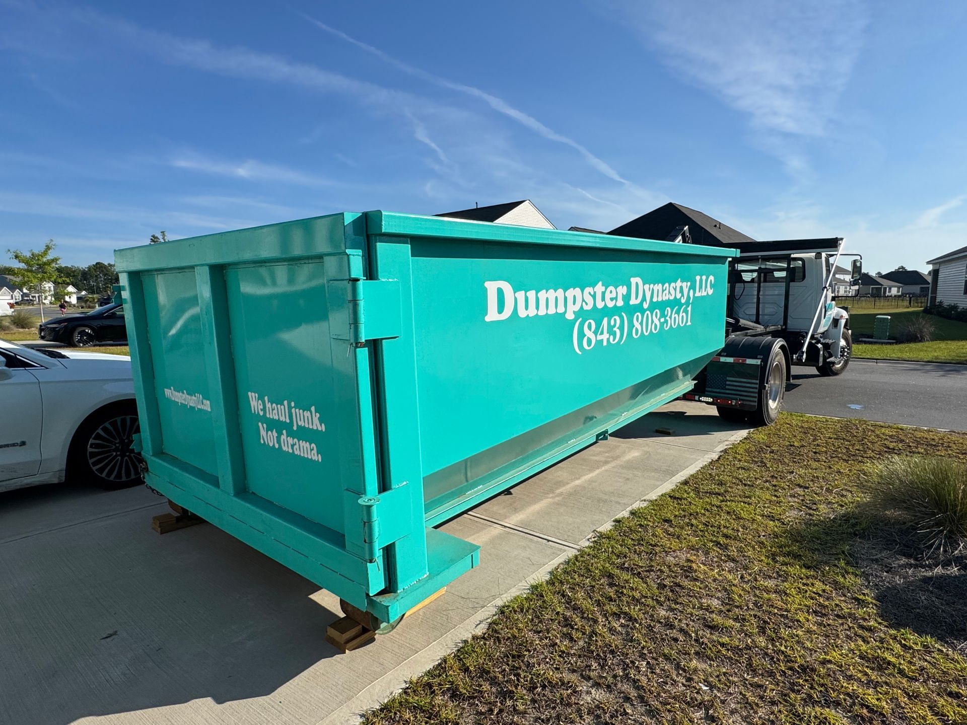 Turquoise Dumpster Today dumpster on a parking lot with a white truck beside it under a blue sky