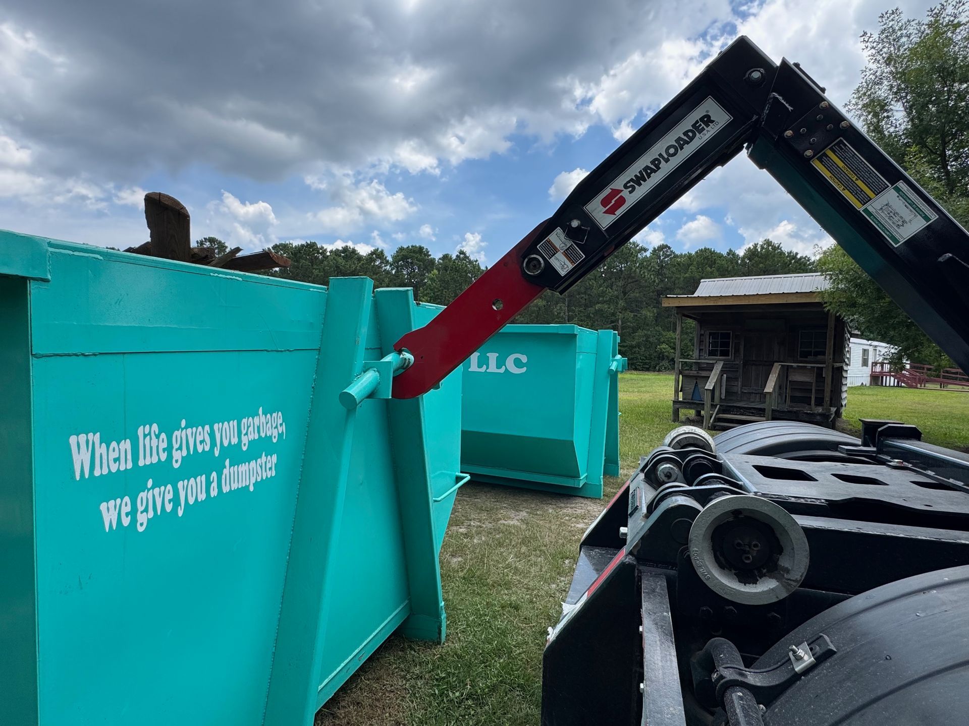 Turquoise concrete barrier with white text beside a red excavator arm and black debris under a cloudy sky