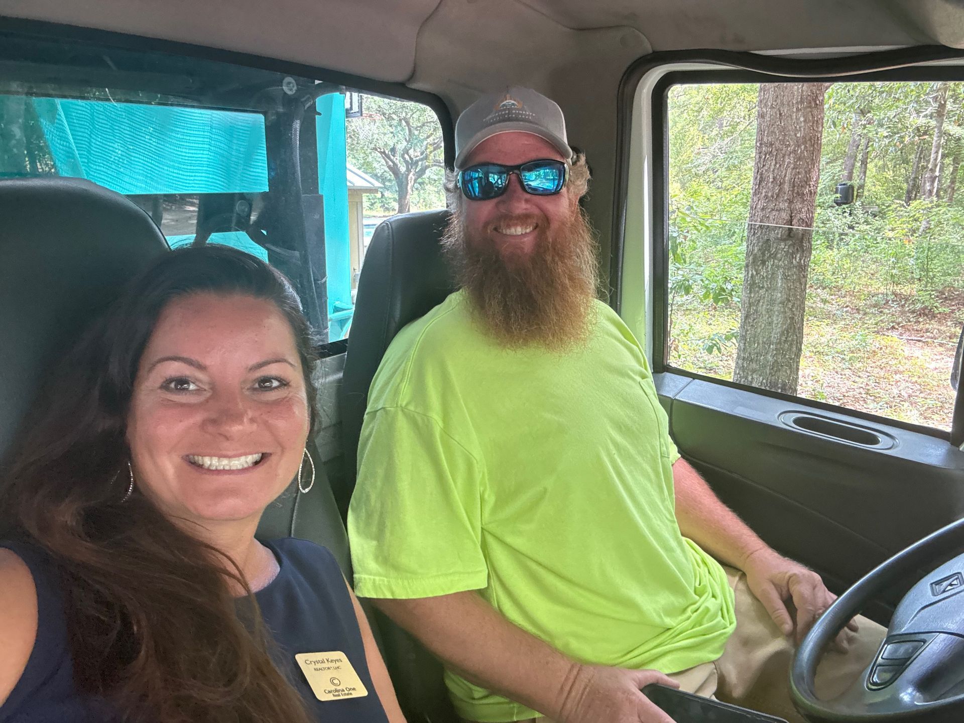 Two smiling people sitting in a golf cart, one in a neon green shirt and blue sunglasses.